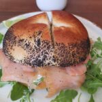 EN A homemade bagel filled with smoked salmon, smooth cream cheese and fresh rocket, served at Artist Cafe in Shoreditch near Old Street. CN 自制贝果，夹有烟熏三文鱼、奶油奶酪和芝麻菜，于 Shoreditch 的 Artist Cafe 提供。 ES Bagel casero con salmón ahumado, queso crema y rúcula, servido en Artist Cafe Shoreditch. FR Bagel maison garni de saumon fumé, fromage frais et roquette, servi à l’Artist Cafe Shoreditch. DE Hausgemachter Bagel mit Räucherlachs, cremigem Frischkäse und Rucola, serviert im Artist Cafe Shoreditch. IT Bagel fatto in casa con salmone affumicato, formaggio cremoso e rucola, servito all’Artist Cafe Shoreditch. JA 自家製ベーグルにスモークサーモン、クリームチーズ、ルッコラを挟んだ一品。Shoreditch の Artist Cafe にて提供。 NL Huisgemaakte bagel gevuld met gerookte zalm, roomkaas en rucola, geserveerd bij Artist Cafe Shoreditch.